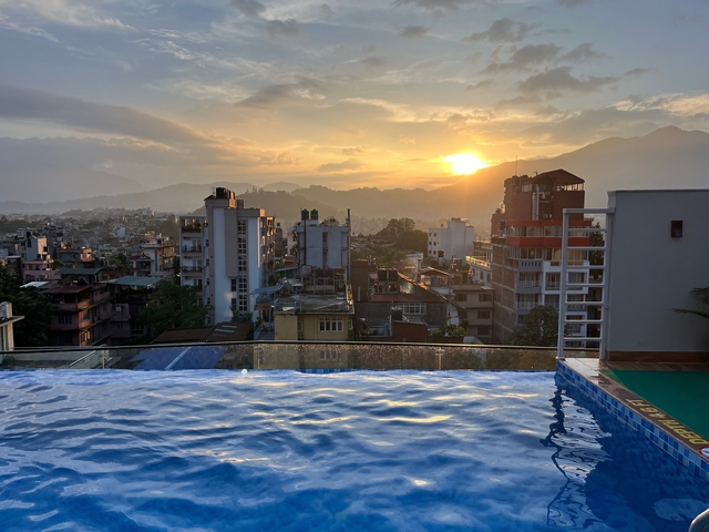       Skyline of a city at sunset with a pool in the foreground.
  