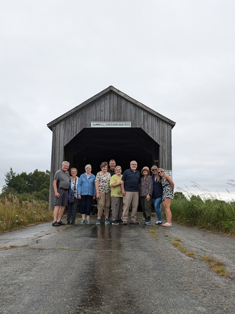 Group of people posing in front of a covered bridge.