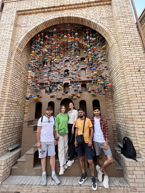 Group of people in front of a wall with colorful hanging decorations.