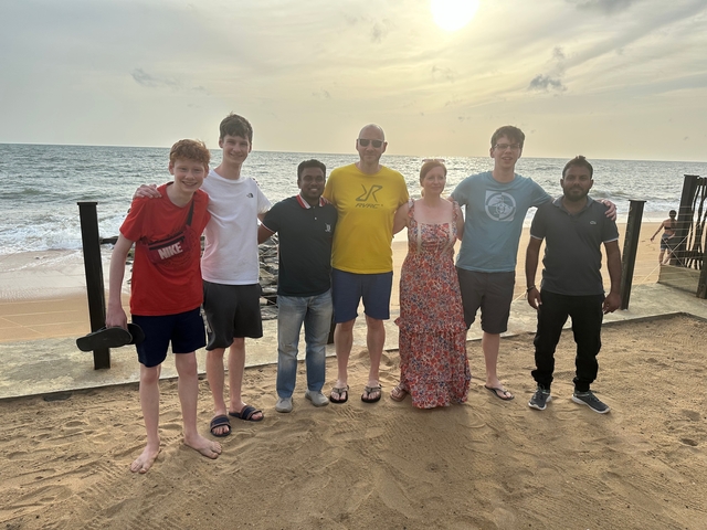 Group photo of people standing on a beach during sunset.