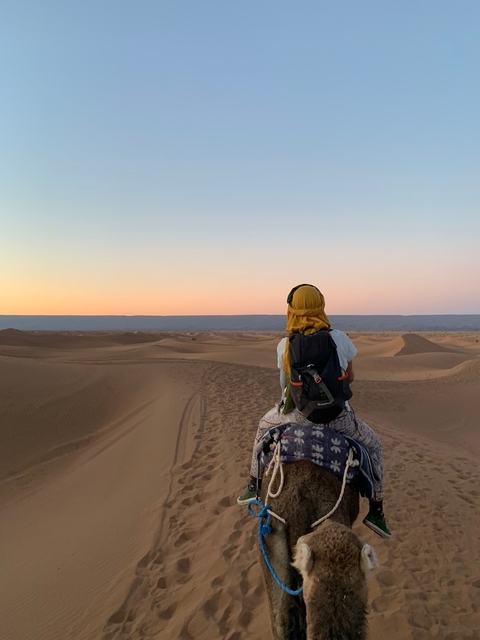 Person riding a camel in desert landscape during sunset.