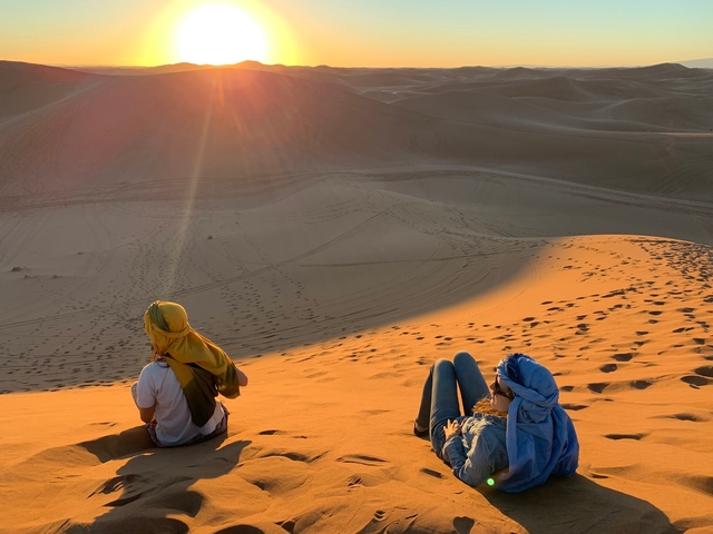       Two people sitting on sand dunes, basking in the sun.
  