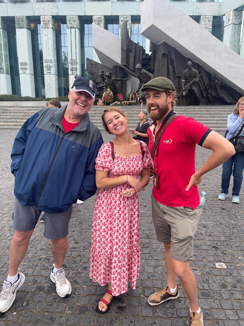 Three people posing outdoors with a statue in the background.