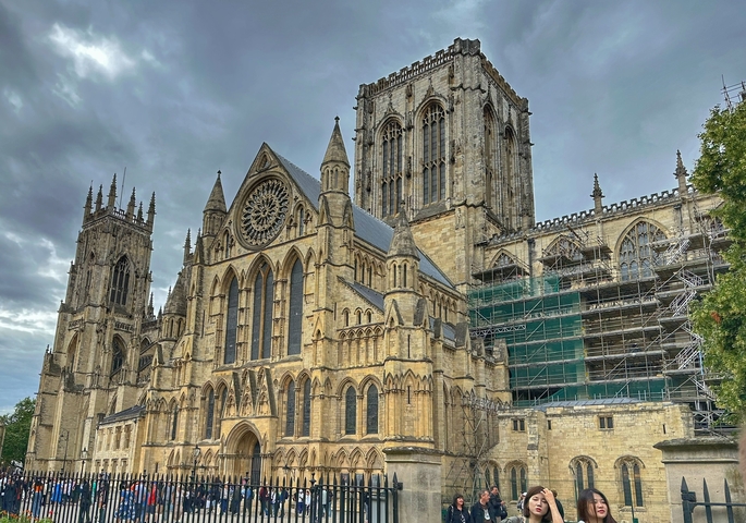       Large Gothic cathedral with intricate architecture under cloudy sky.
  