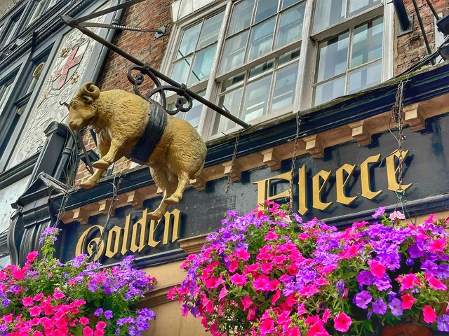       Exterior of a pub with a hanging golden fleece sign and flowers.
  