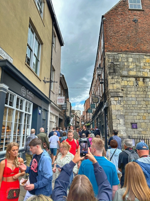 Busy narrow street with shops and people walking around.
