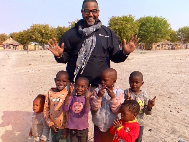 Group of children and a man in a village setting.