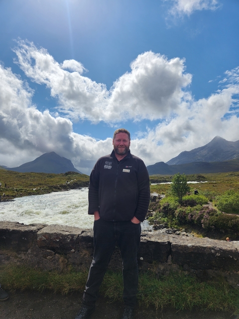 Person standing in front of mountains and river.