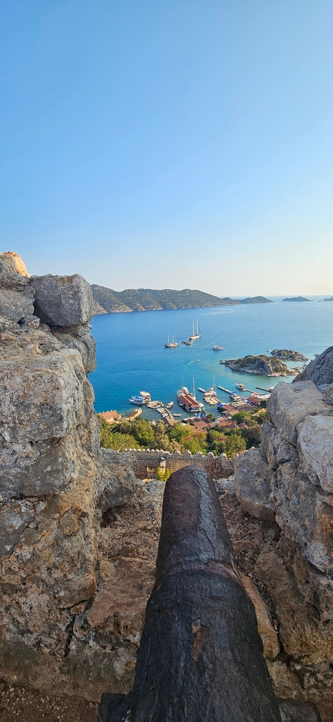       View of a harbor with boats and blue water from a rocky vantage point.
  