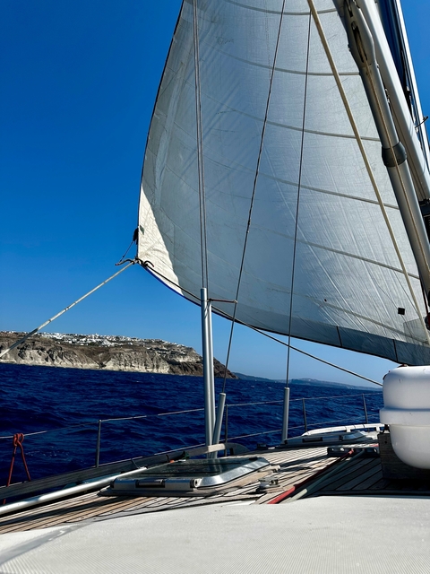       Sailing view with a sail and coastal cliffs in the distance.
  
