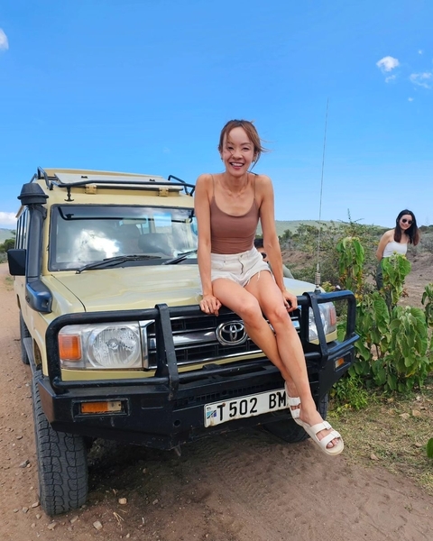Person sitting on the hood of a safari vehicle with sparse vegetation around.