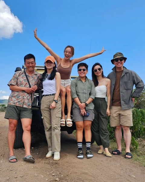 Six people posing in front of a safari vehicle in a natural setting.