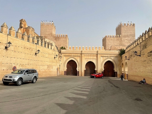       Historical gates with cars in a plaza area.
  