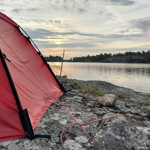 Red tent setup by a rocky lakeside during sunset.