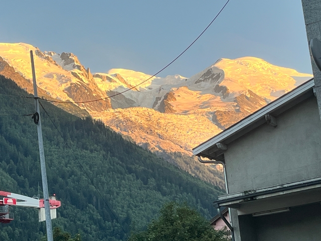Mountains with snow-covered peaks illuminated by golden sunlight, seen from a small town.
