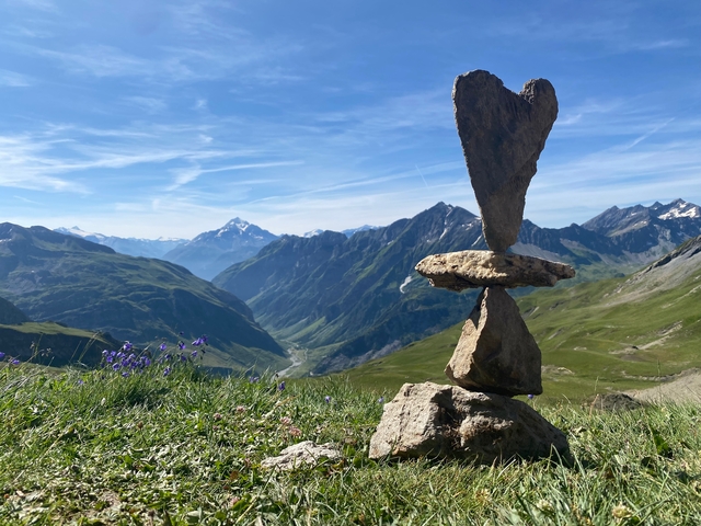       Balanced rock formation on top of a hill with mountains in the distant background.
  