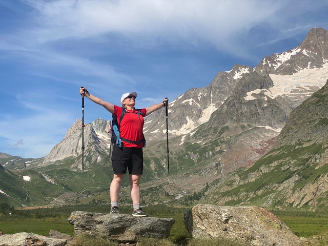 A lone hiker triumphantly raising arms amidst a majestic mountain landscape.