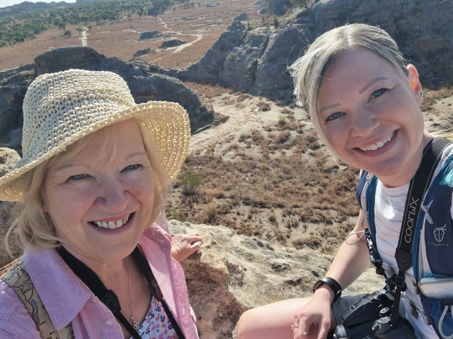       Two women posing on rocky terrain with dry landscape behind.
  