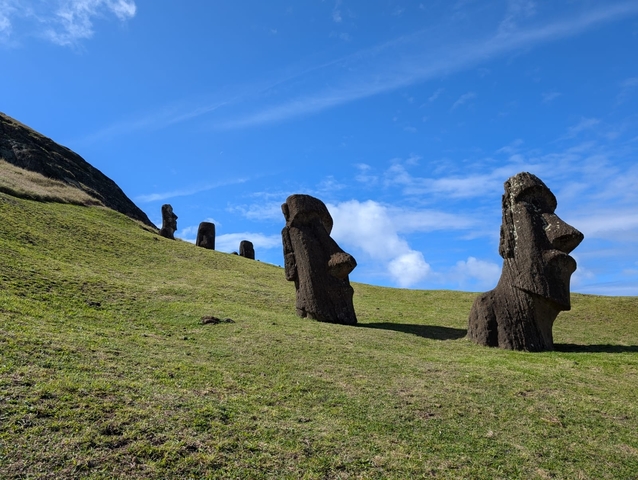 Moai statues on a grassy hillside under a clear sky.