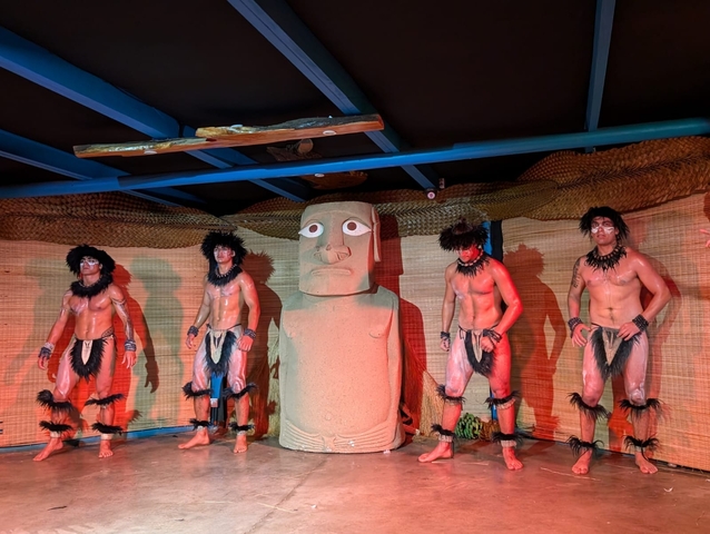       Performers on stage with a large Moai statue in view.
  