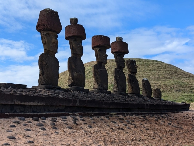 Line of Moai statues with hats on a hilltop.