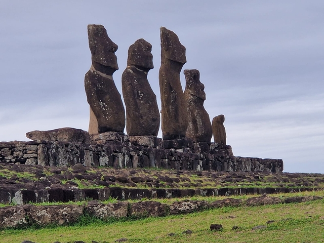 Group of Moai statues on a raised platform under a cloudy sky.