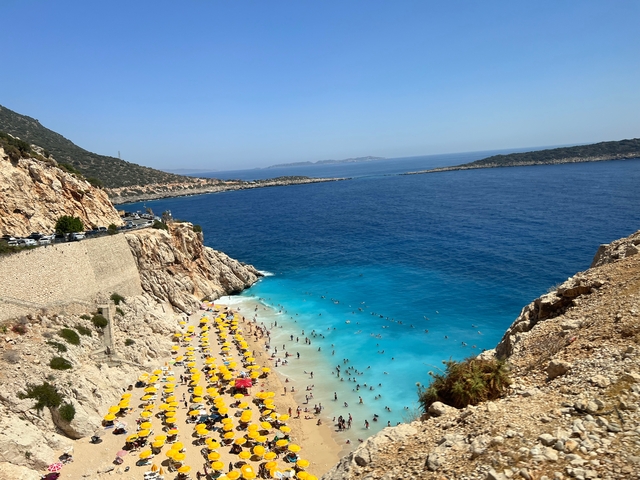 Crowded beach with parasols, blue sea, and cliffs.