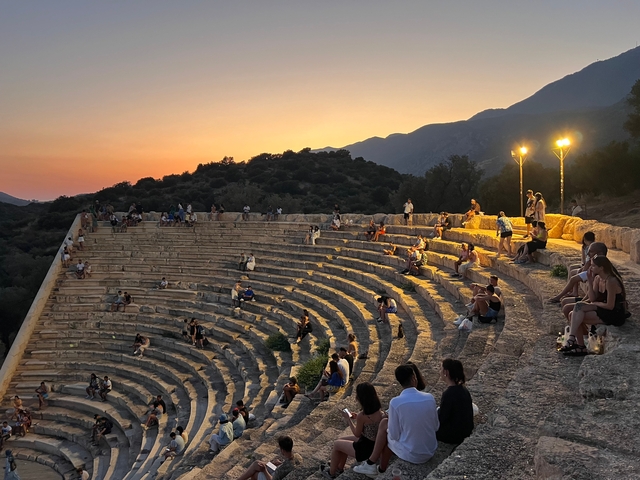Amphitheater with people seated, lit during sunset.