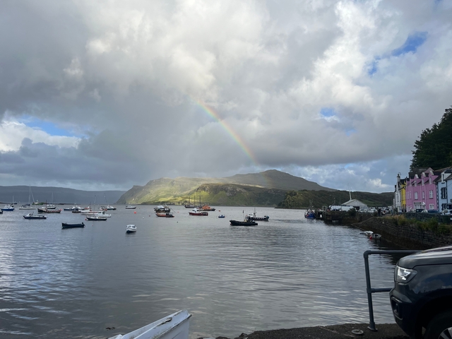 Boats moored in a harbor with a rainbow in the distance.