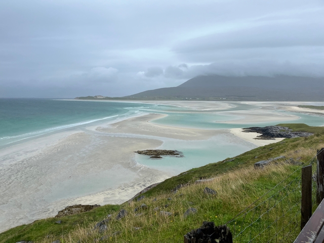 A scenic view of a beach with sand bars and mountains in the background.