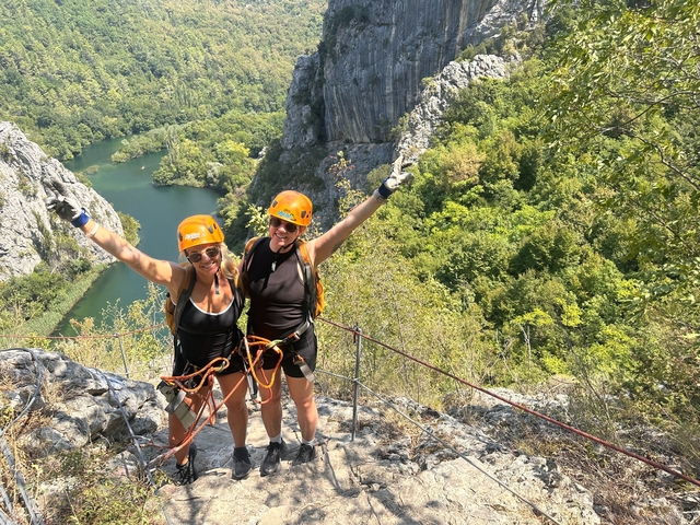       Two people with helmets and harnesses celebrating on a mountain.
  