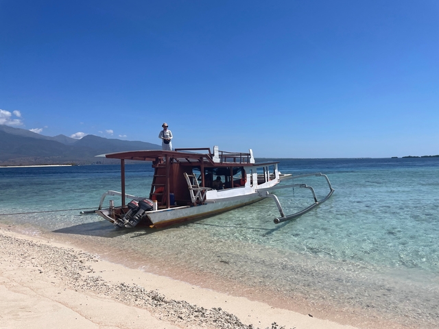       A person on a boat near a beach with clear water.
  