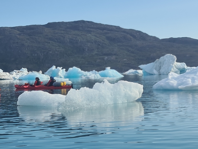       Kayakers paddling near iceberg in a serene setting.
  