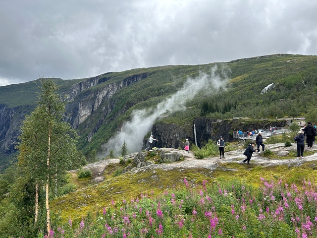       Hikers enjoying a lush mountainous landscape with waterfalls.
  