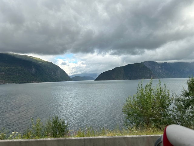       Calm Norwegian fjord surrounded by mountains and cloudy sky.
  