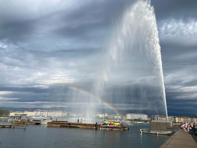 Large water fountain with rainbow against cloudy sky.