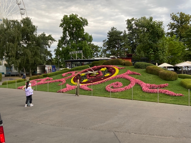 Large floral clock with people nearby in a park setting.