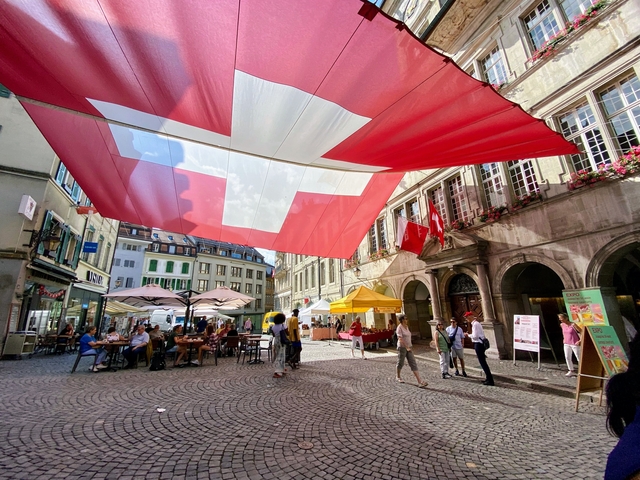 A street market under large Swiss flags.