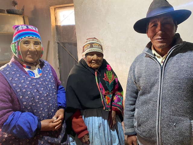       Three people wearing traditional Andean clothing indoors.
  