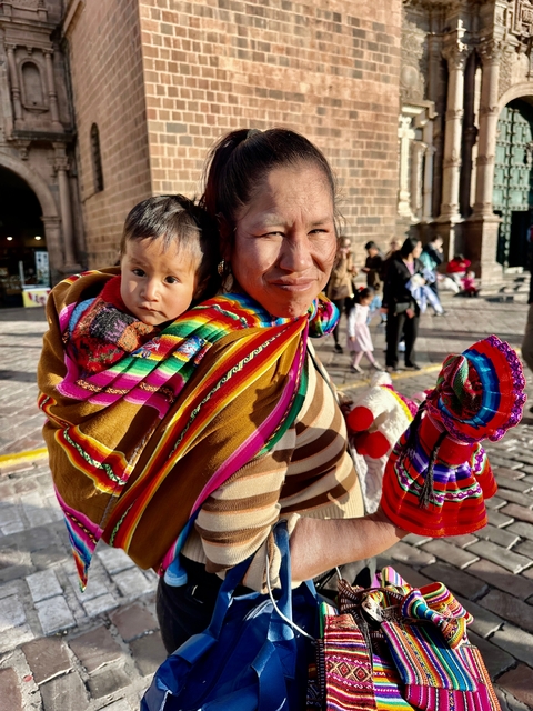       Woman carrying a baby wrapped in colorful fabric.
  