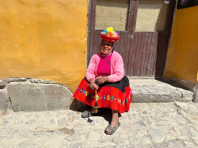       Woman in traditional clothing sitting by a yellow wall.
  