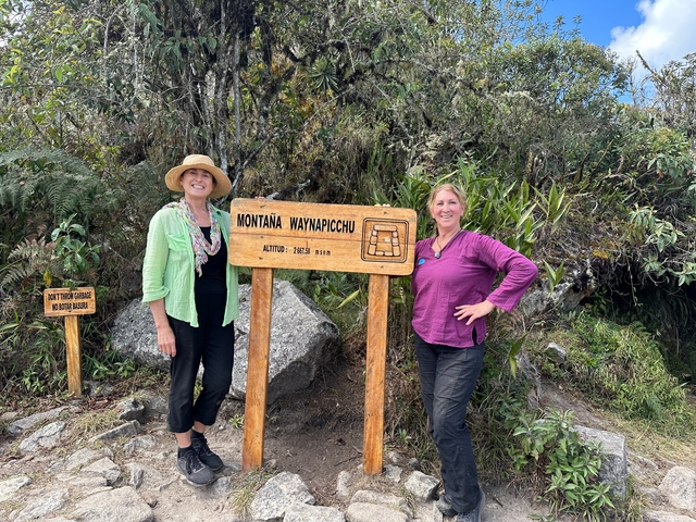       Two women posing next to a sign for Montaña Wayna Picchu.
  