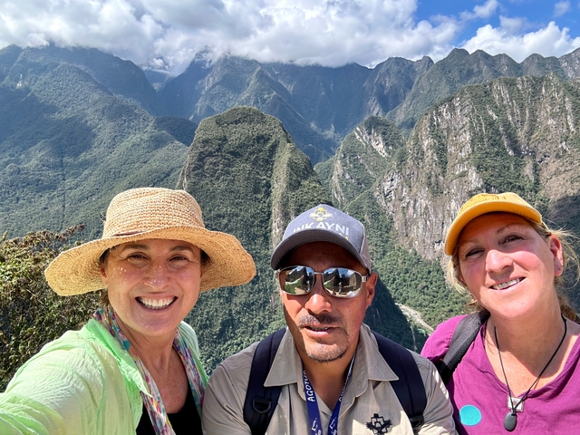       Three people posing with mountainous landscape in the background.
  