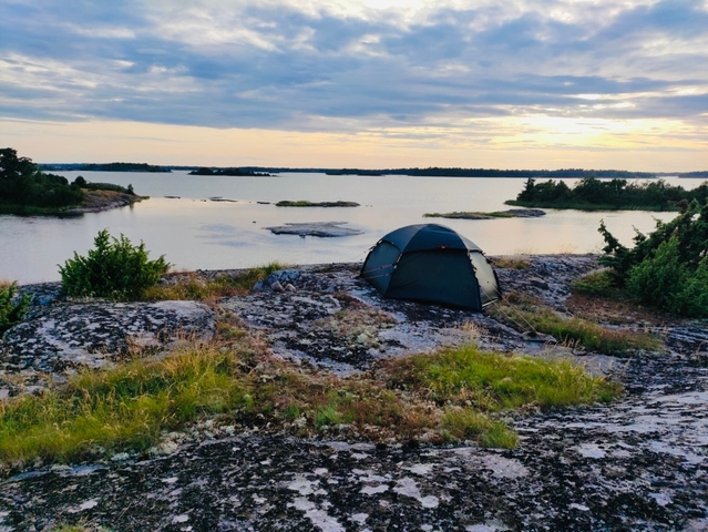 Tent pitched on rocky terrain by a serene coastline.