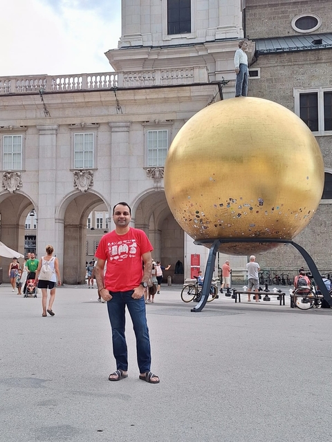       Man posing in front of a large golden globe in a public square.
  