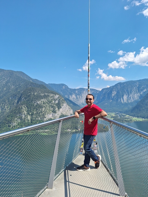       Man posing on a lookout with a scenic mountain and lake view.
  