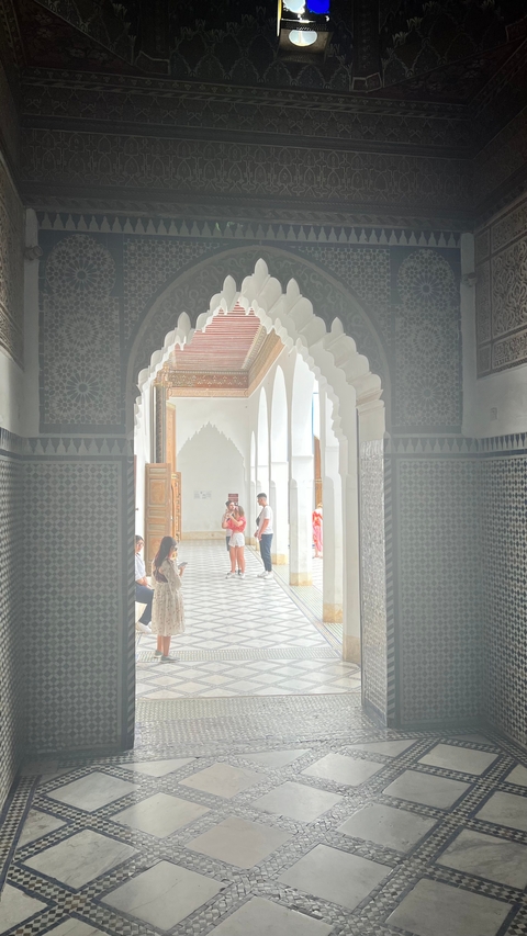       Interior of a palace with people walking; arches and tiles are visible.
  
