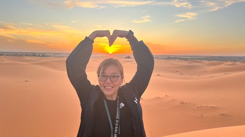       Person making a heart shape with their hands against a sunset in the desert.
  