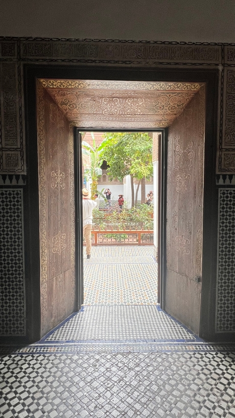      People taking photos in a garden seen through ornate doors.
  