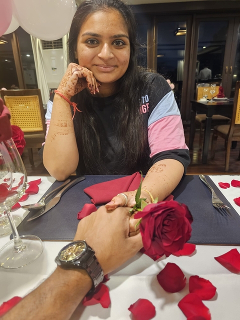       Person holding a rose with candles and napkins on a table.
  